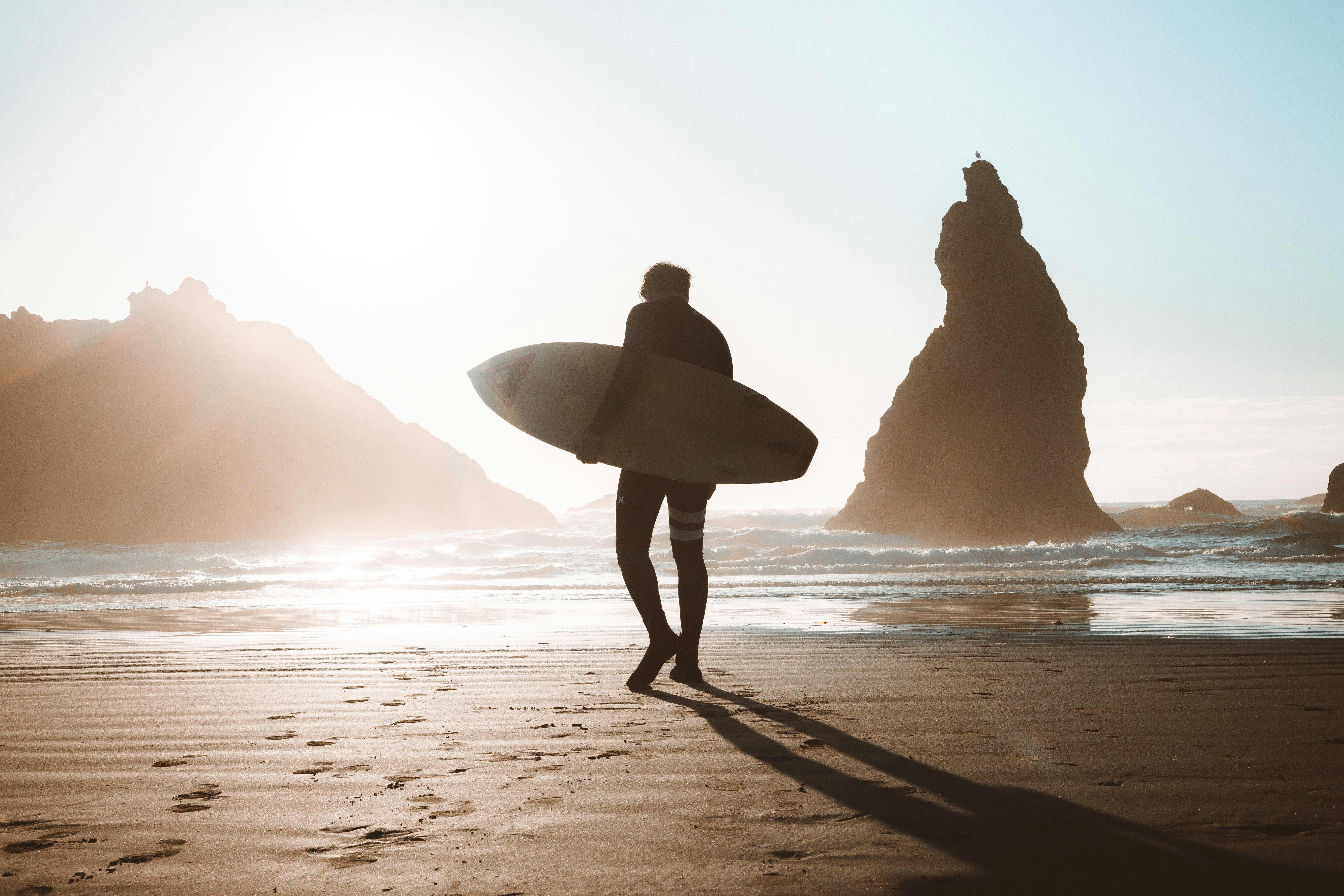 silhouette of person holding white surfboard walking on beach during sunset